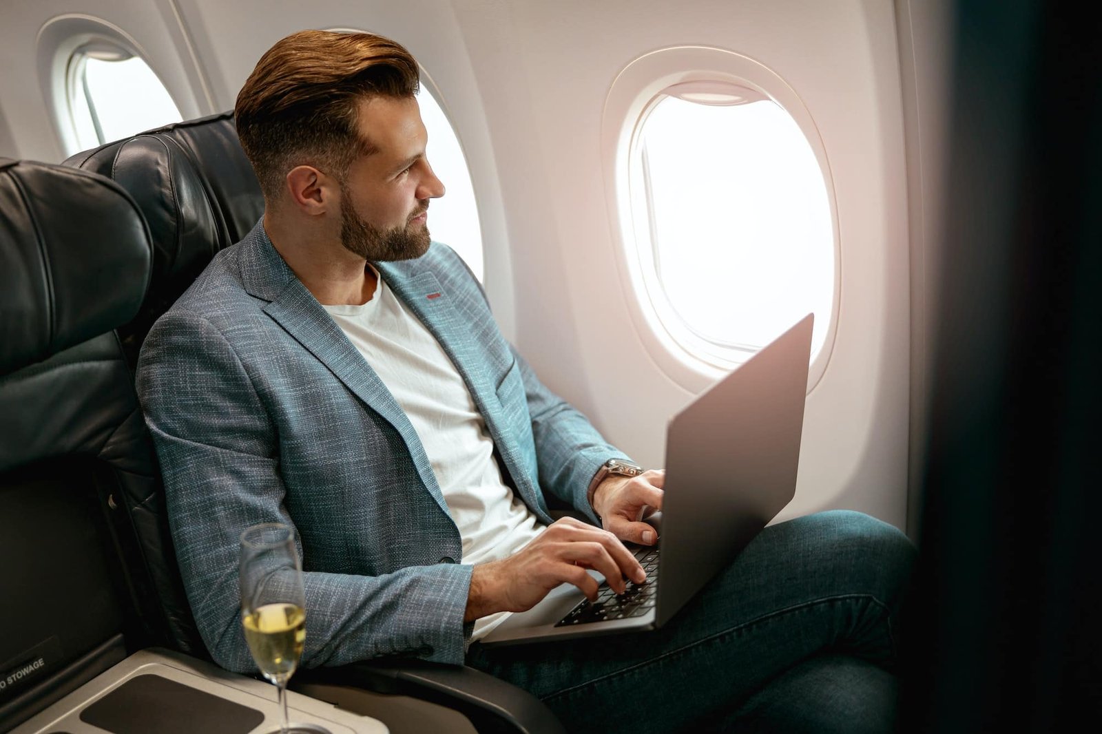 Suited man holding a laptop and looking outside the window of an Empty Leg Private Jet