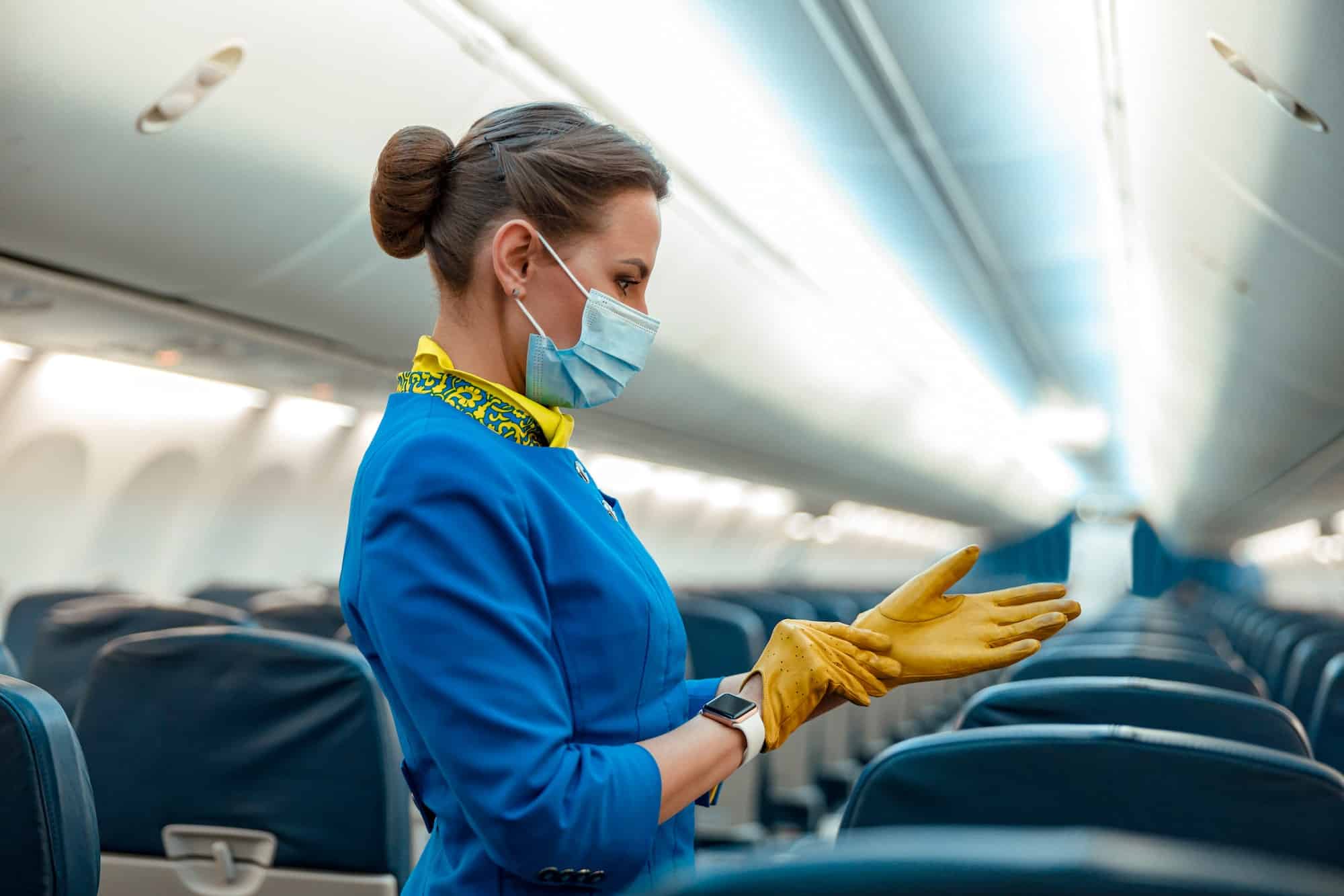 Stewardess in medical mask putting on gloves in airplane