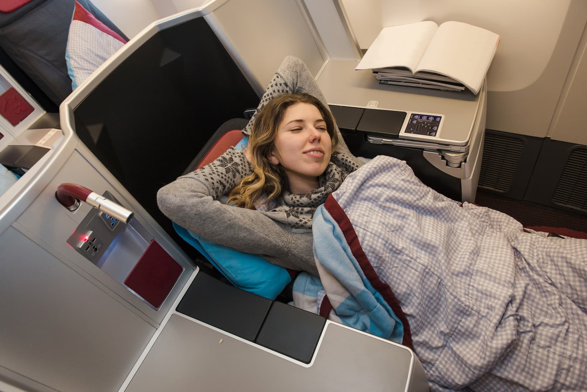 Woman passenger sleeping at the business class of airplane in comfortable single seat. Flight at fir