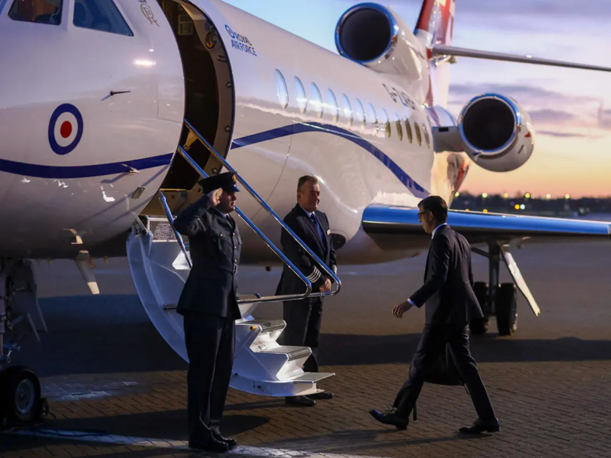 Guard saluting the man in a coat, holding a suitcase and about to enter the private plane