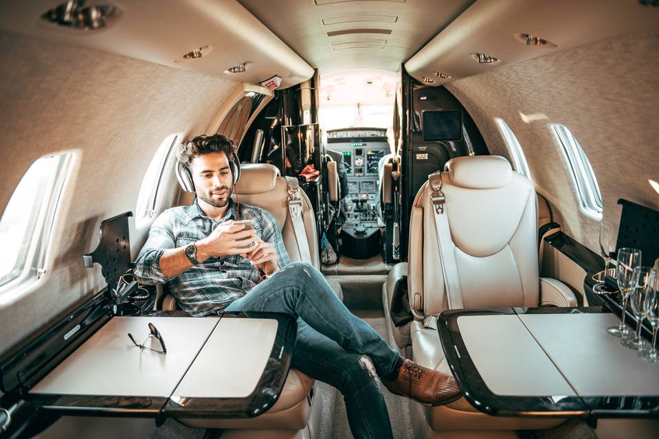 Smart boy in a shirt and pants listening to music on headphones in a private plane