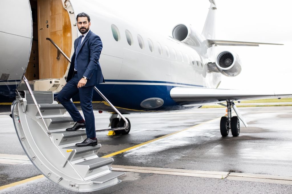 Man in a blue coat looking back while standing on the stairs of the private plane
