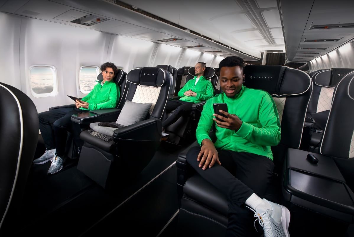 Two male and one female sports players in green uniforms seated in a private jet.