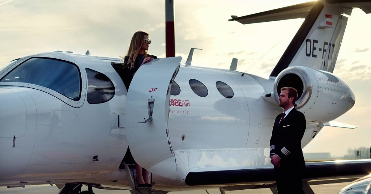 woman-in-sunglasses-standing-on-the-door-step-of-a-private-jet-with-a-pilot-standing-beside-it.